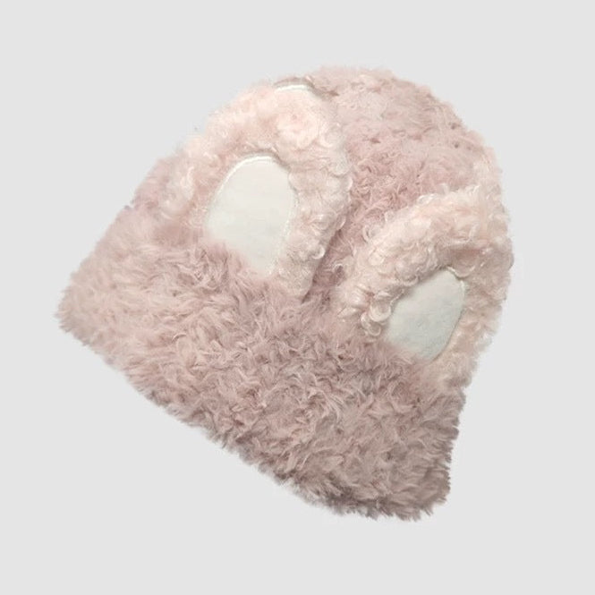 Pink plush hat with white accents on a light gray background, featuring branding text.